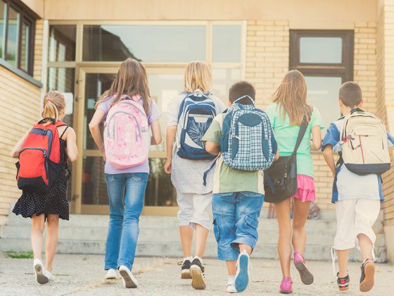 Groupes d'enfants avec sac à dos devant une école